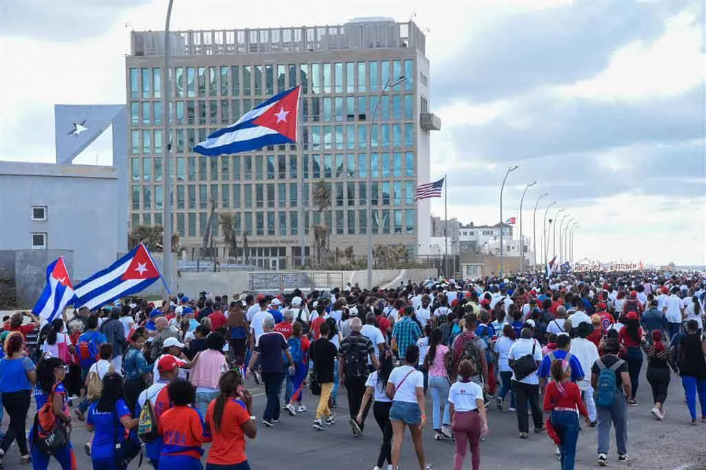 Demonstration with Cuban flags in front of a modern building, American flag also visible.